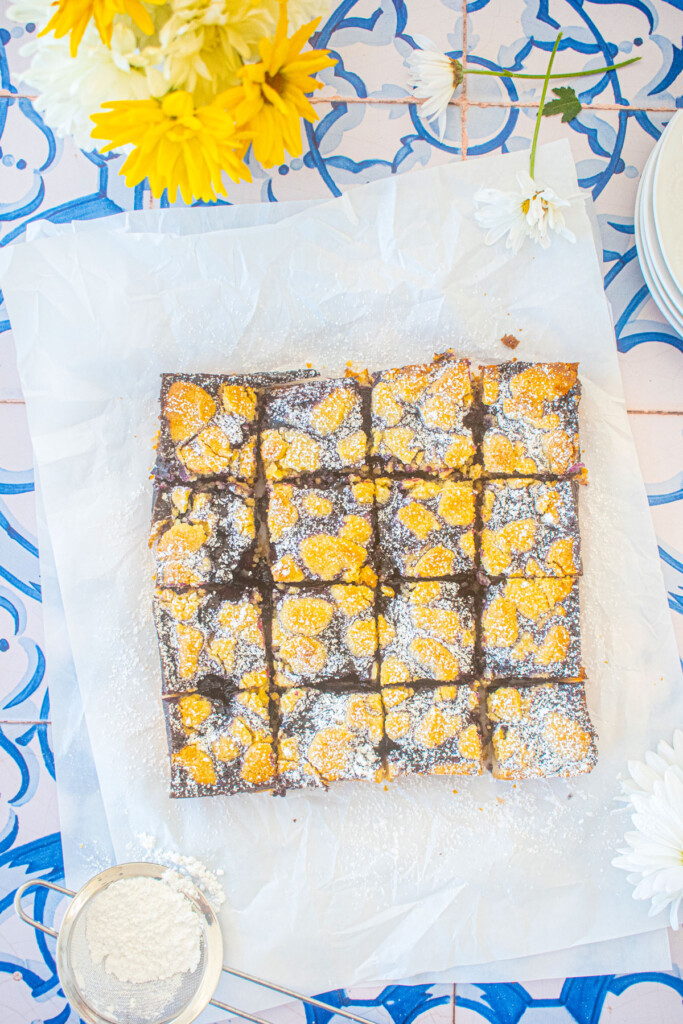 sourdough blueberry crumb bars cut into 16 squares on white parchment paper on a blue tile table.