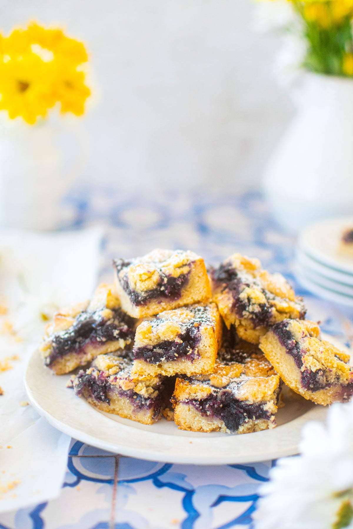 sourdough blueberry crumb bars on a plate on a blueberry tile table with fresh flowers.