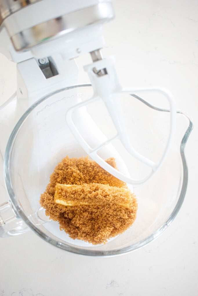 butter and brown sugar in a glass mixing bowl on a white marble counter.