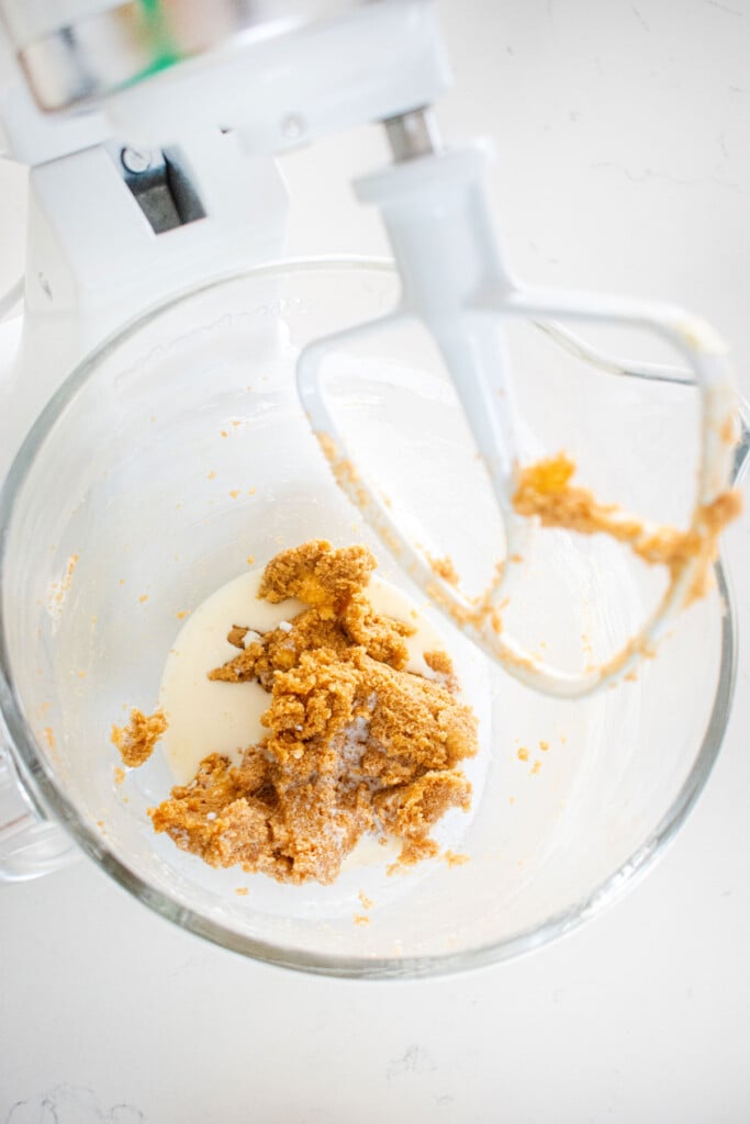 creamed butter and sugar with milk in a glass mixing bowl on a white marble counter.