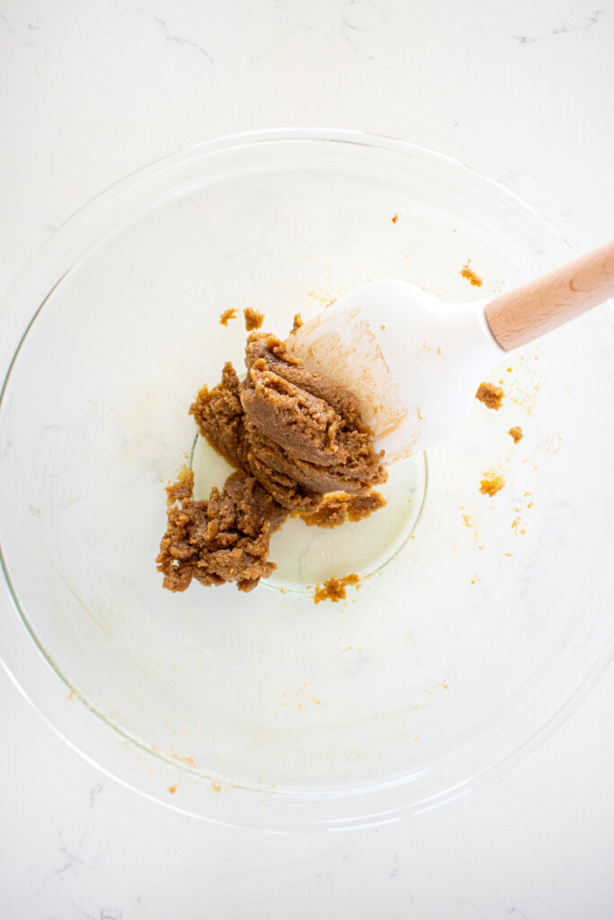 butter and brown sugar mixed together in a glass mixing bowl on a white marble counter.