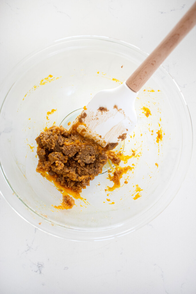 brown sugar and butter mixed with pumpkin in a glass mixing bowl on a white marble counter.
