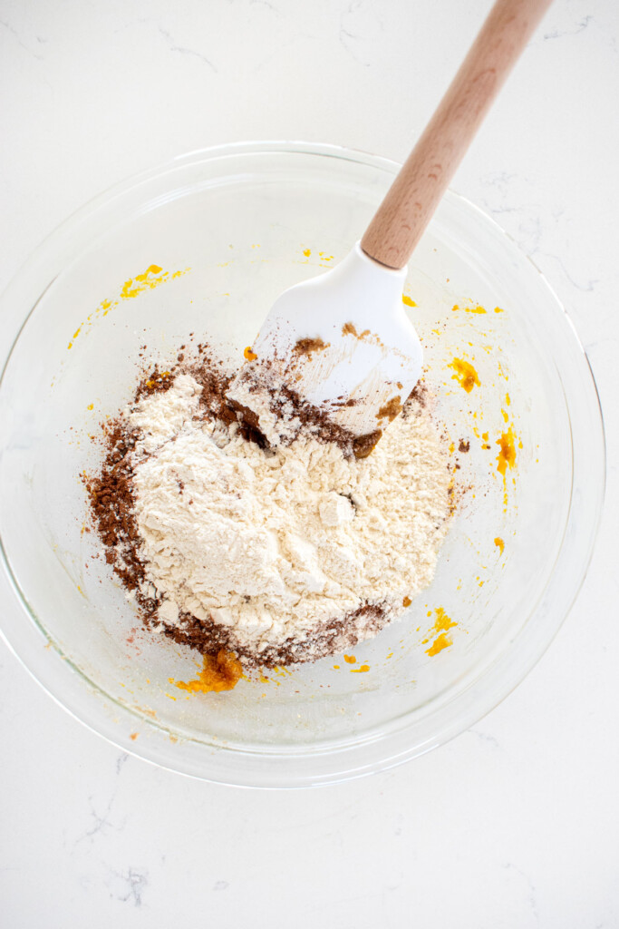 ingredients for one big chocolate cookie in a glass mixing bowl on a white marble counter.