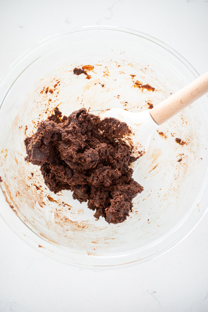 chocolate cookie dough in a glass mixing bowl on a white marble counter.
