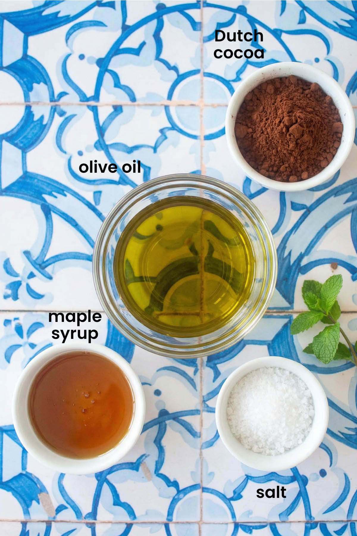 individual ingredients for chocolate olive oil caramel sauce laid out against a blue tile background.