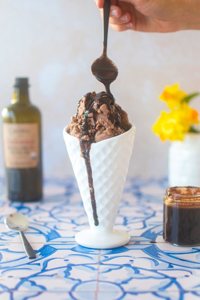 chocolate olive oil caramel sauce being poured over chocolate ice cream in a dish on a blue tile counter.