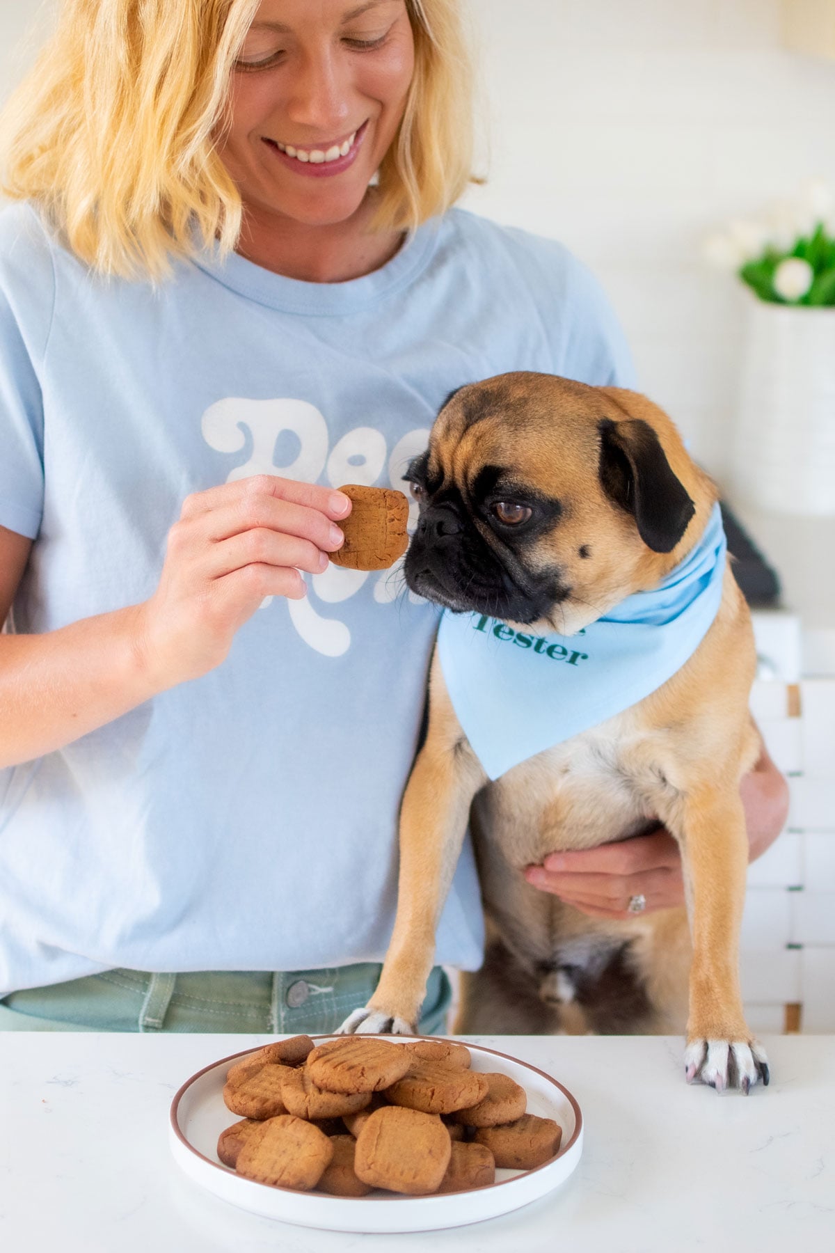 woman feeding pug a mushroom peanut butter dog treat at the kitchen counter.