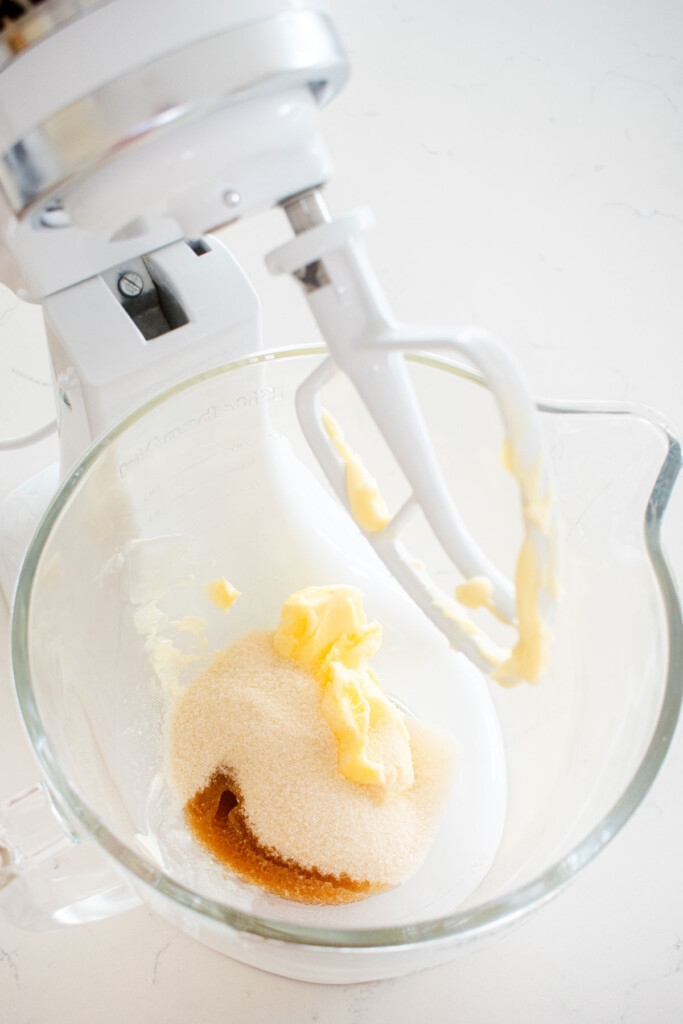 butter sugar and vanilla in a glass mixing bowl on a white marble counter.