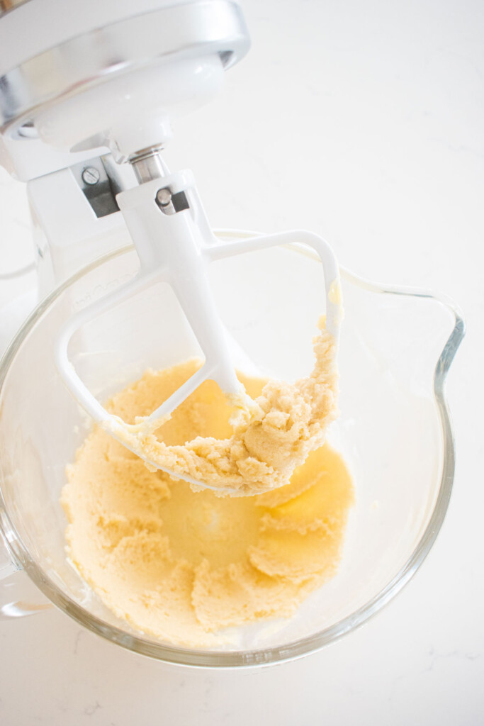 creamed butter and sugar in a glass mixing bowl on a white marble counter.