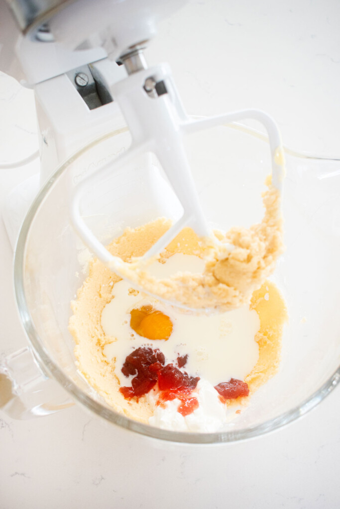 wet ingredients being added to strawberry snack cake batter in a glass mixing bowl on a white marble counter.