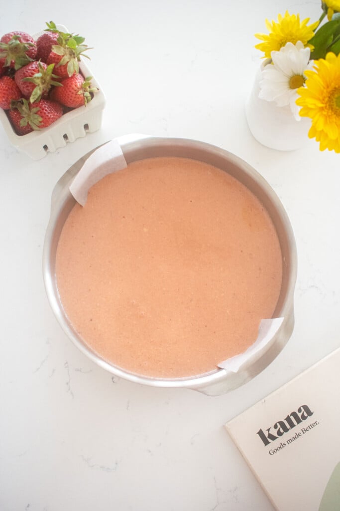 strawberry cake batter in a stainless steel baking pan on a marble counter with fresh berry basket of strawberries.