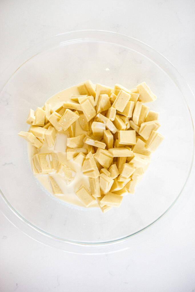 white chocolate and cream in a glass mixing bowl on a marble counter.