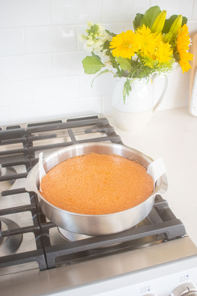 strawberry cake in a cake pan cooling on top of an oven.