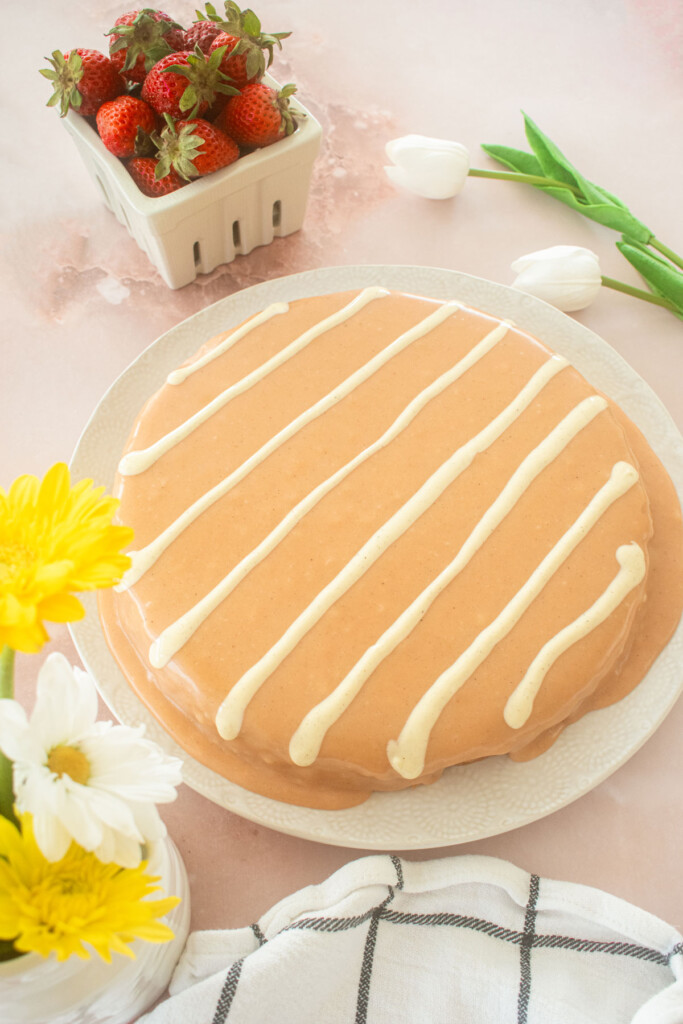 pink cake with white chocolate stripes on a white plate on a pink table.