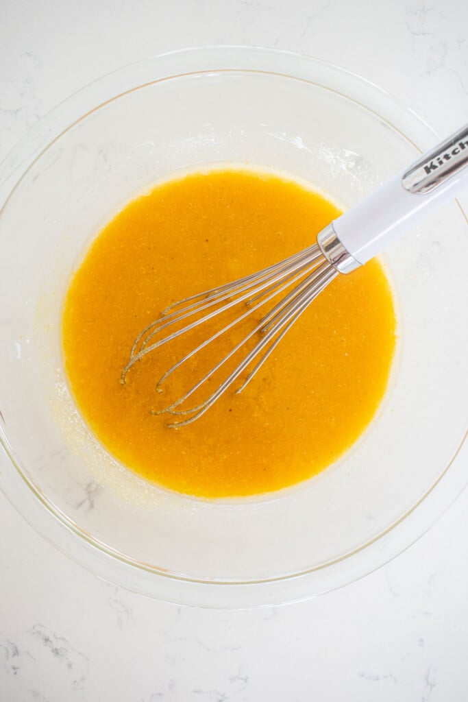vegan chocolate cupcake batter being mixed with a whisk in a glass bowl on a marble counter.