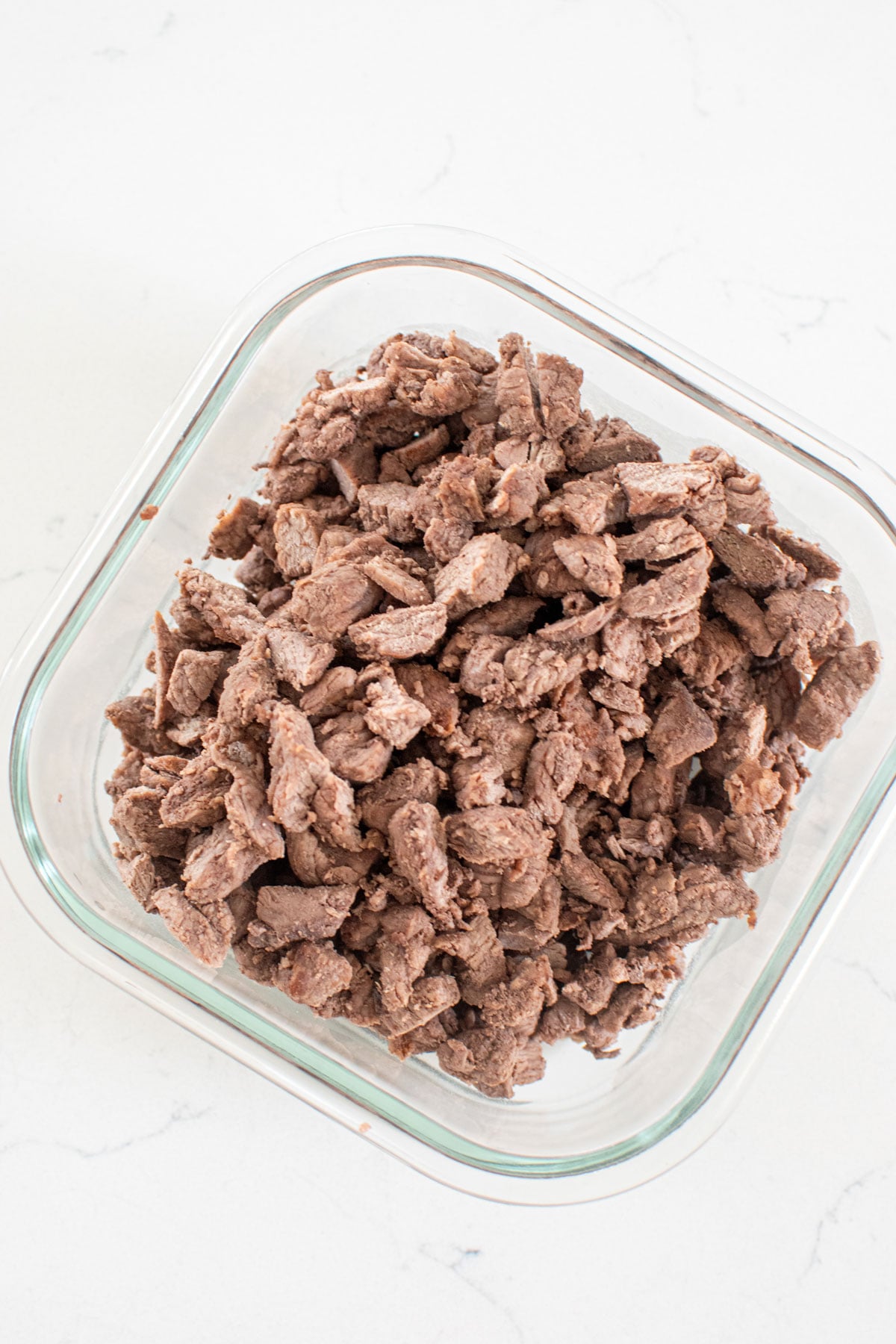 beef dog treats cut into small pieces in a glass tupperware on a white kitchen counter.