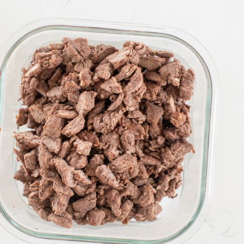beef dog treats cut into small pieces in a glass tupperware on a white kitchen counter.