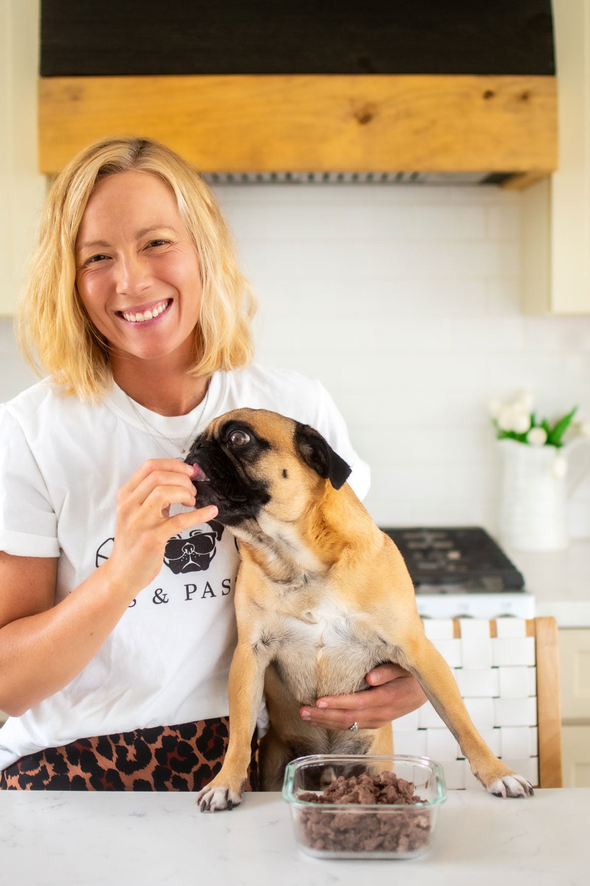 woman feeding a pug beef dog treats at the kitchen counter.