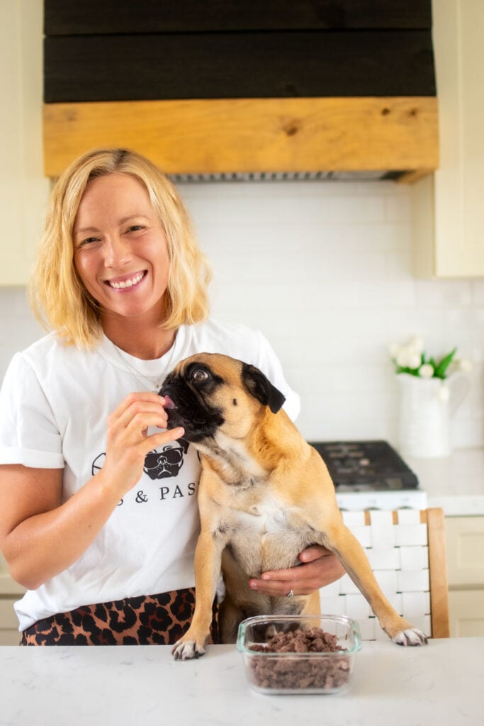 woman in kitchen feeding pug beef dog treats