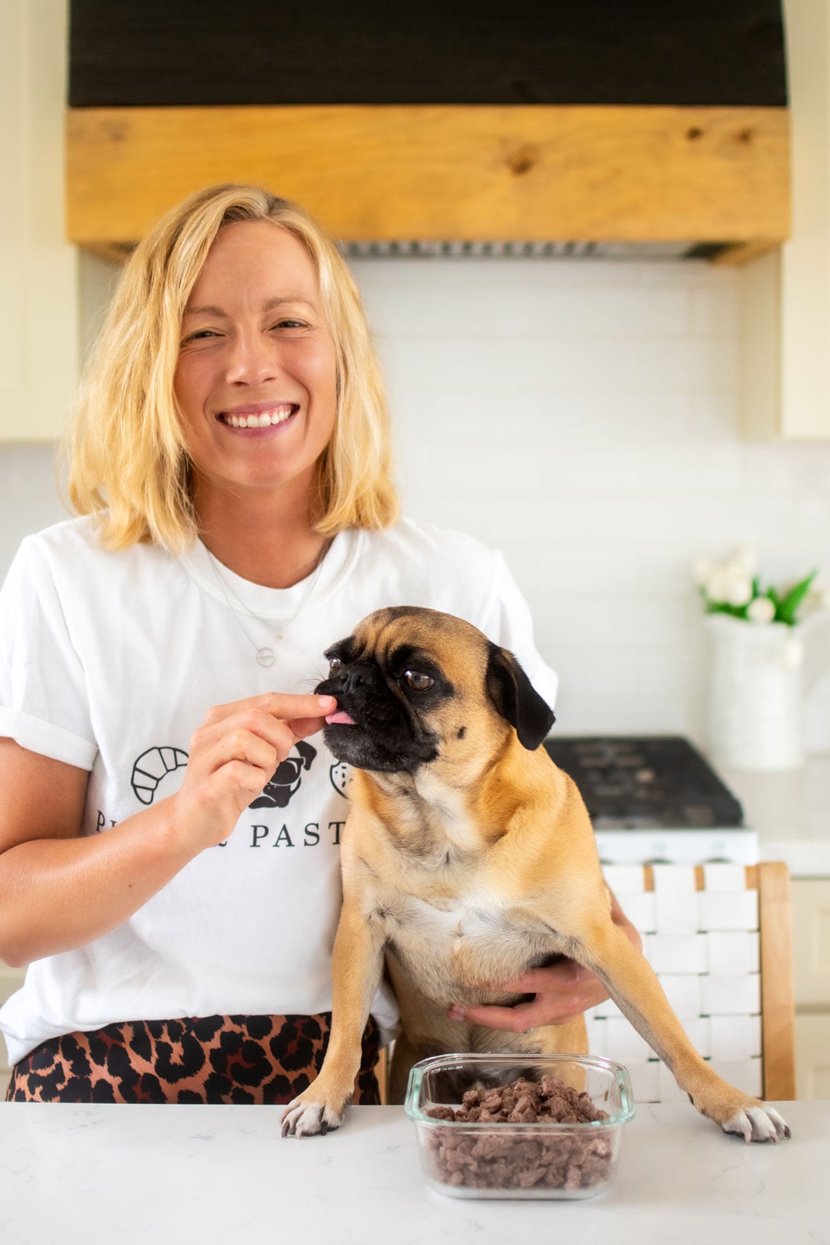 woman feeding a pug beef dog treats at the kitchen counter.