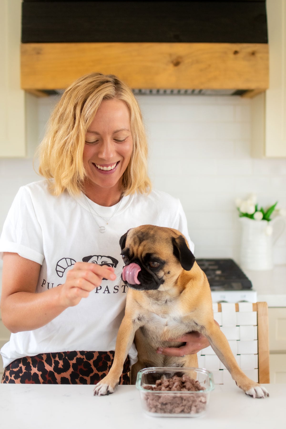 woman feeding a pug beef dog treats at the kitchen counter.