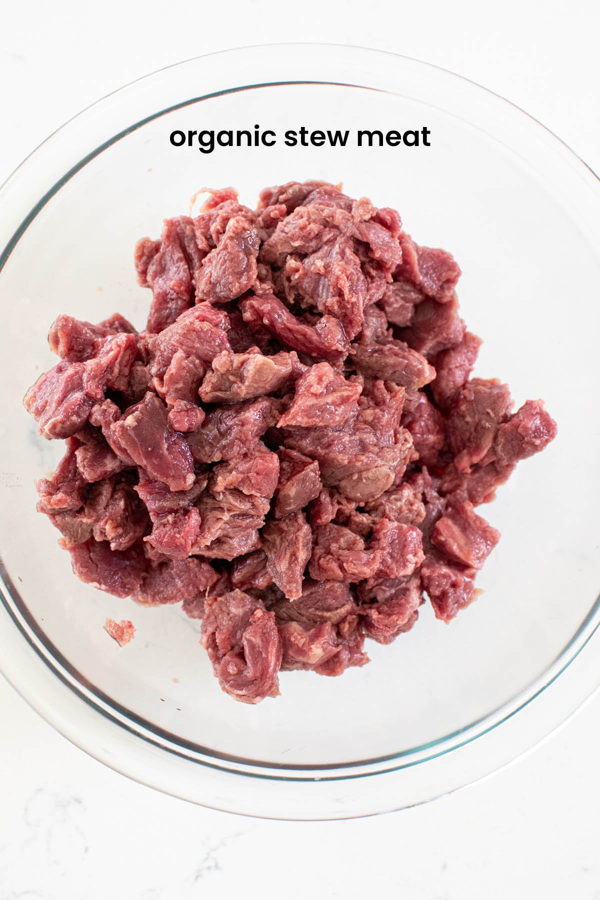 organic stew meat in a glass bowl on a white countertop.