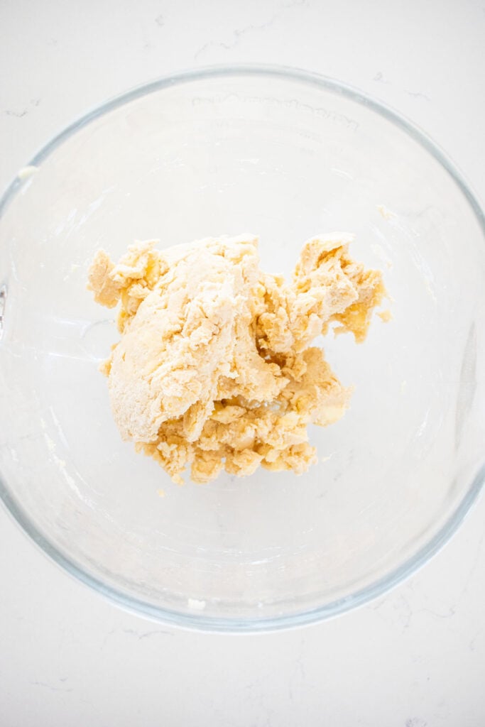pie dough in a glass mixing bowl on a white marble countertop.