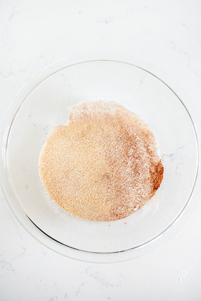 sugar and cinnamon in a glass mixing bowl on a white marble countertop.