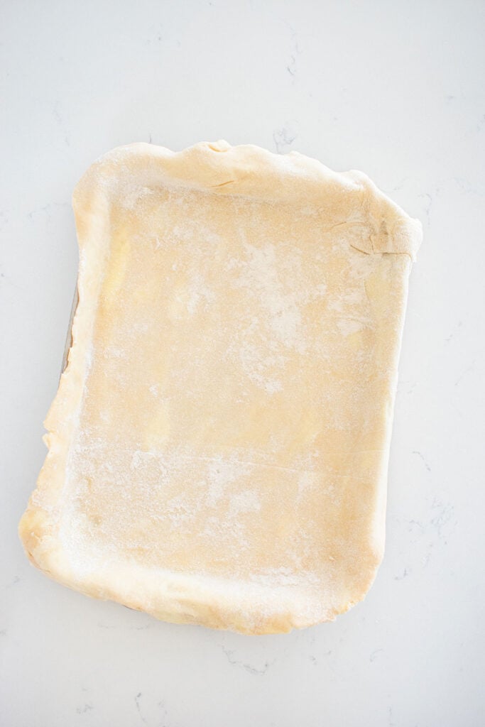 pie crust in a quarter sheet pan on a white marble countertop.