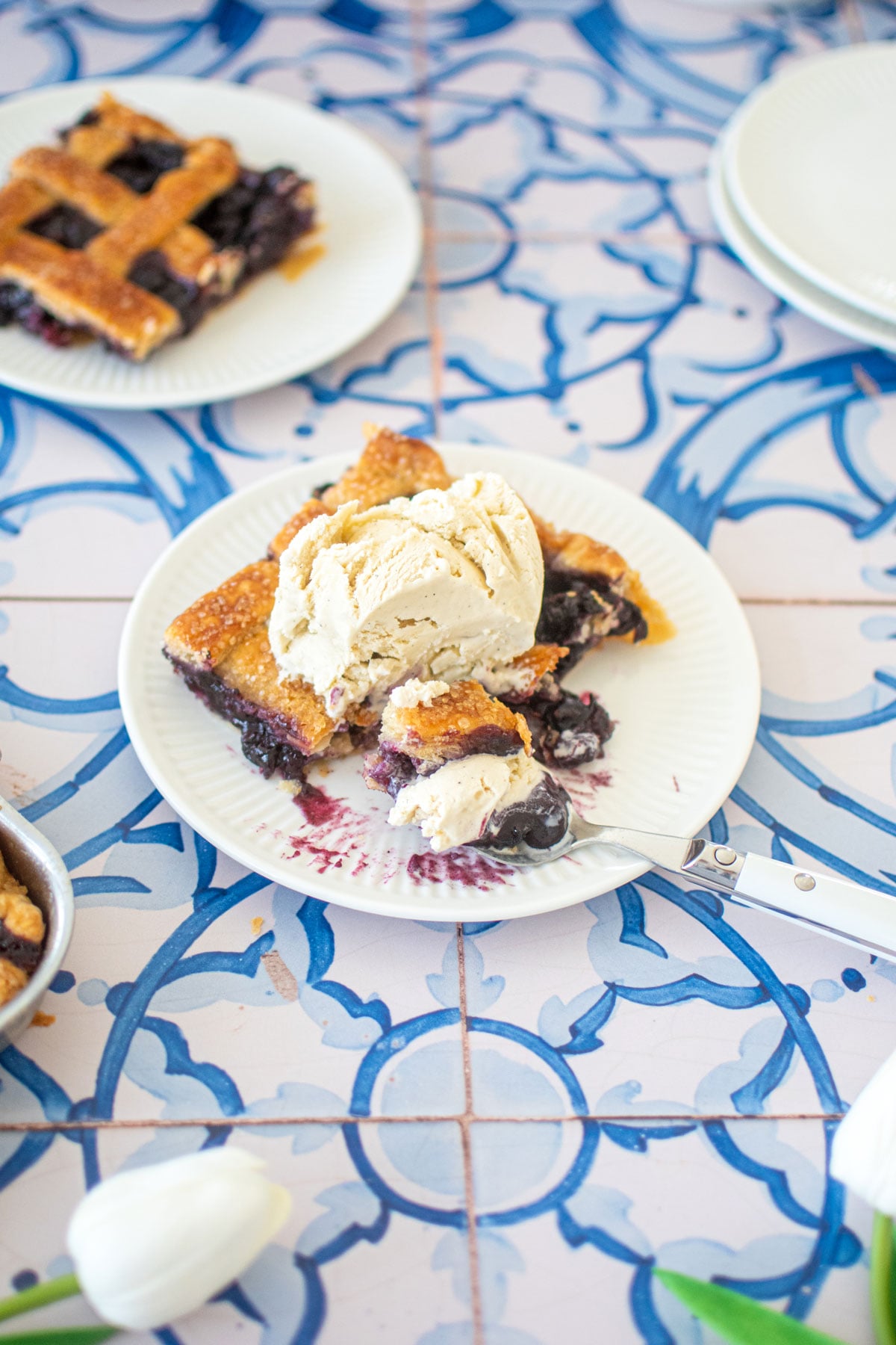 blueberry slab pie without eggs on a plate with a scoop of vanilla ice cream on a blue tile table.