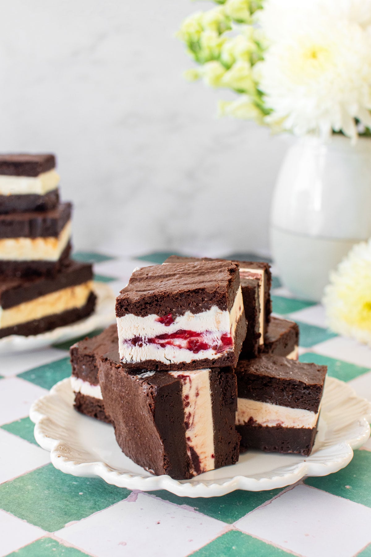 olive oil brownie ice cream sandwiches cut into squares on a plate on a green and white tile table.