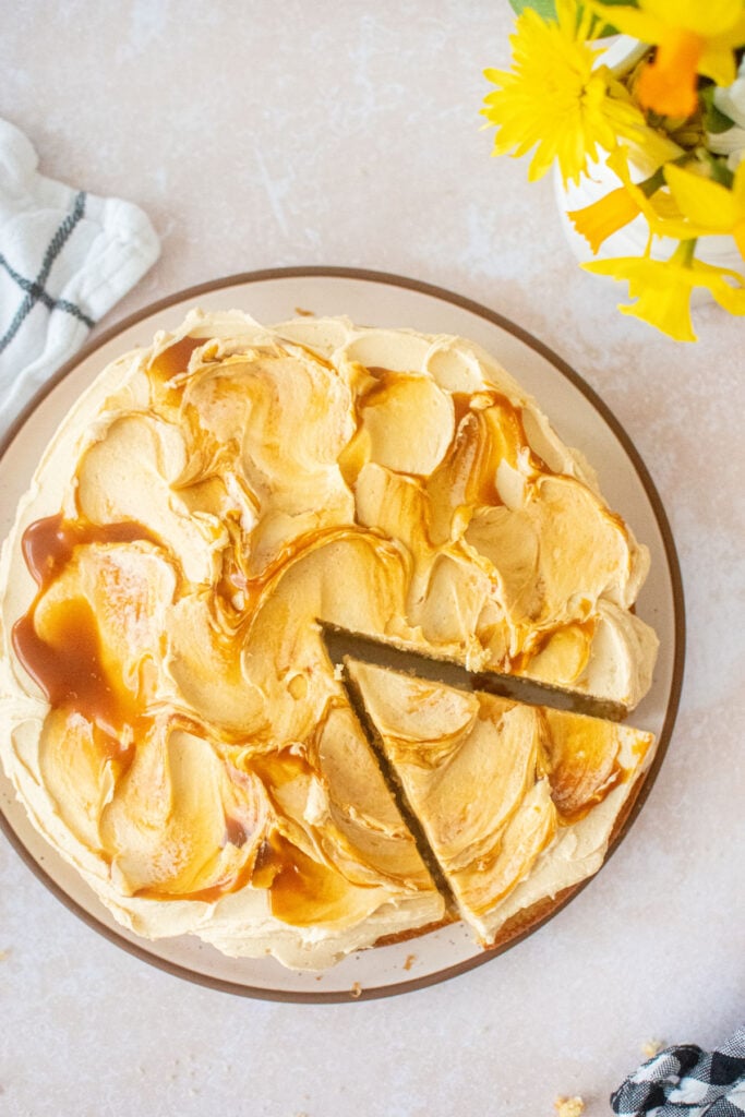 caramel buttercream frosting on vanilla cake on a plate with one slice cut out.