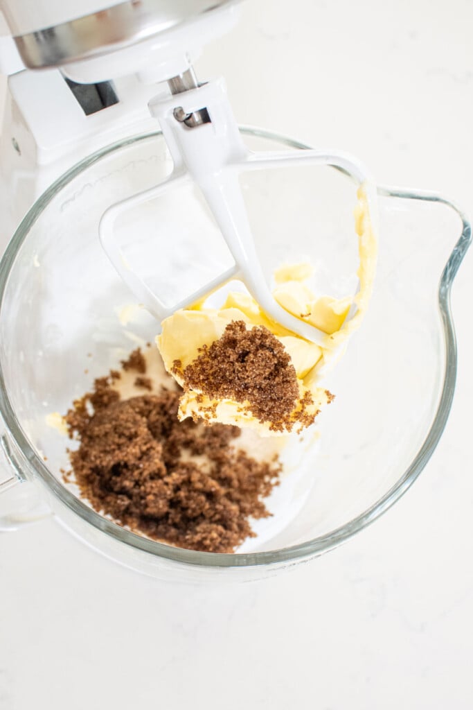 butter, sugar, and dark brown sugar in a glass mixing bowl on a white marble countertop.
