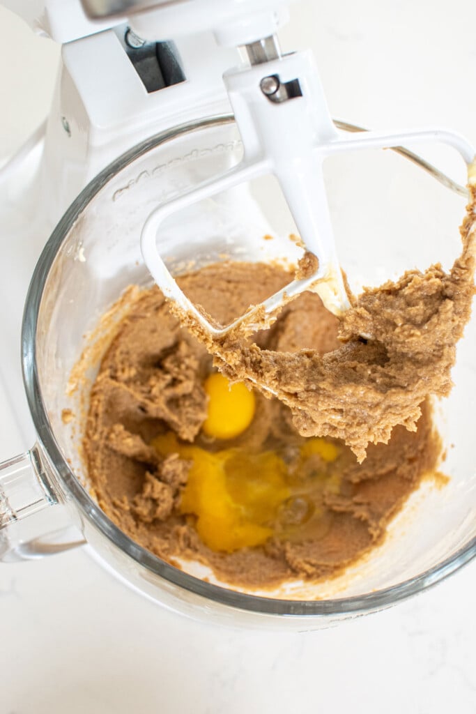 creamed butter and sugar with eggs in a glass mixing bowl on a white marble countertop.