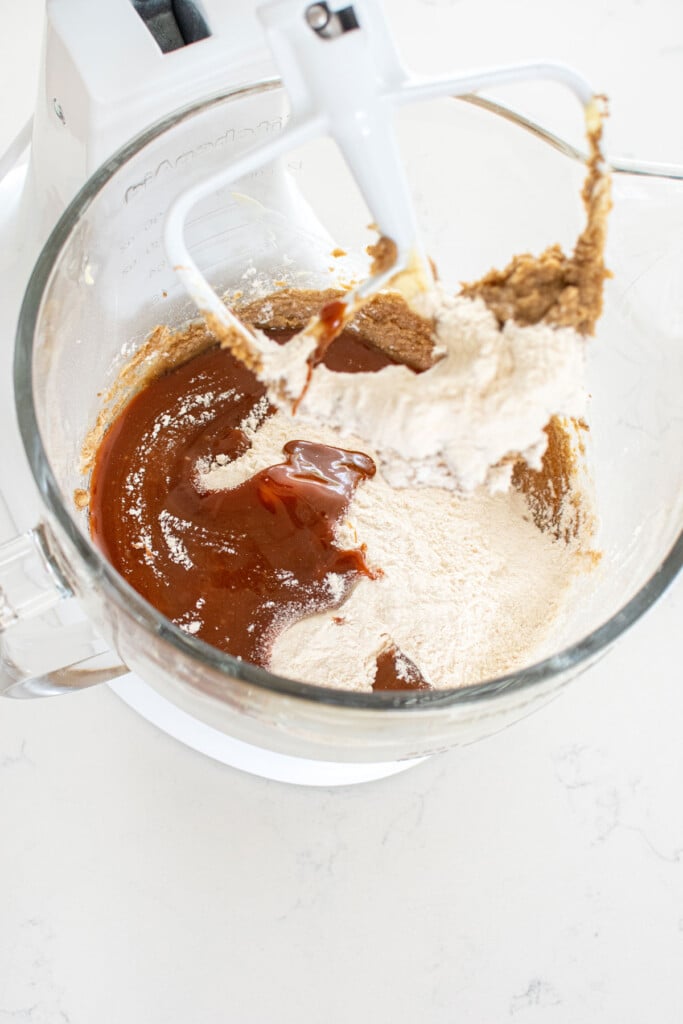caramel cookie dough being made in a glass mixing bowl on a white marble countertop.
