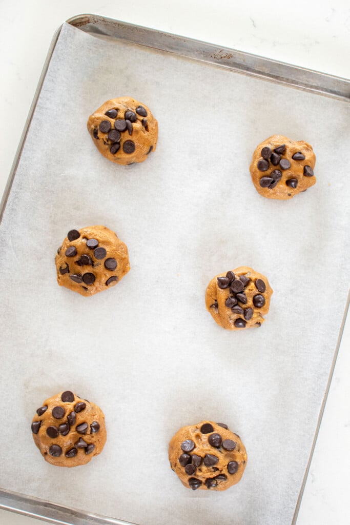 caramel chocolate chip cookie dough on a baking sheet on a white marble countertop.