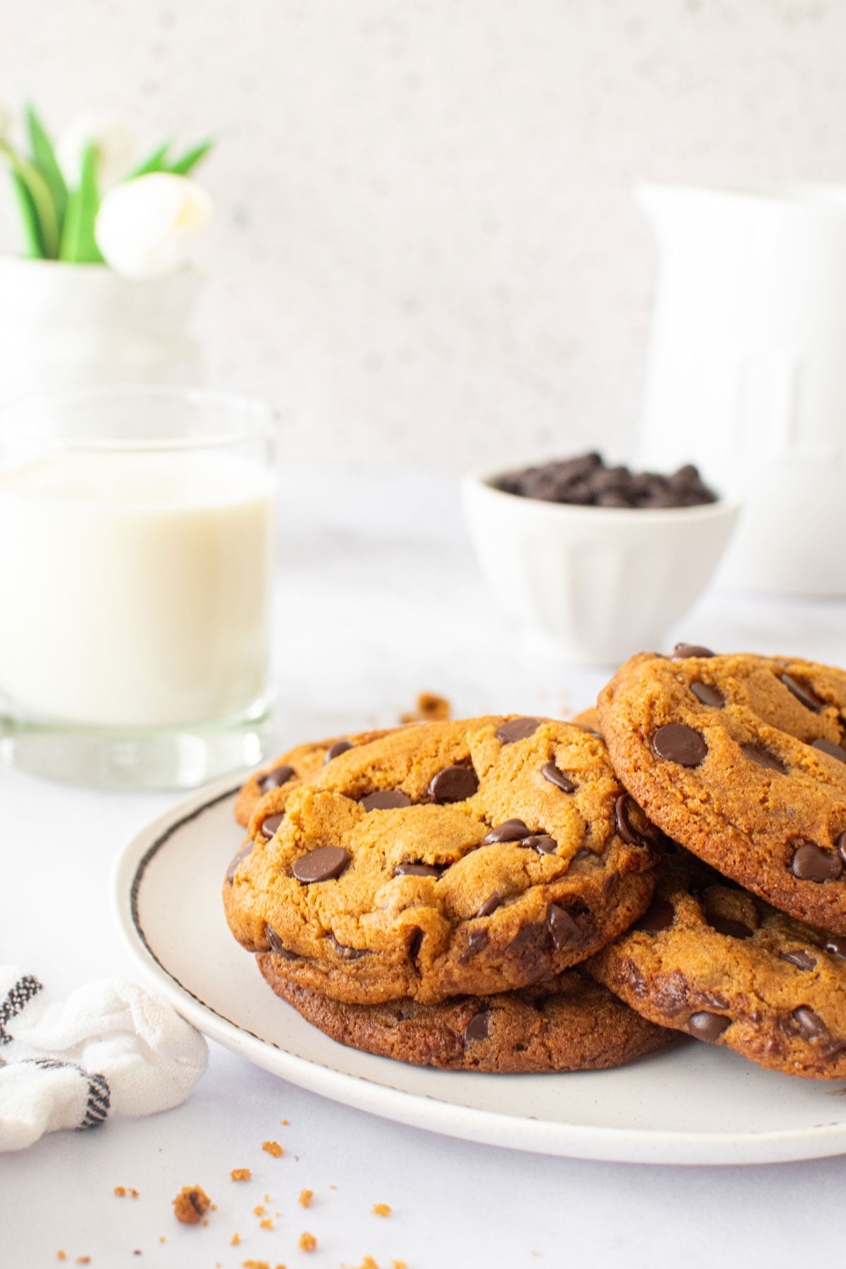 caramel chocolate chip cookies on a plate with a glass of milk on a white countertop.