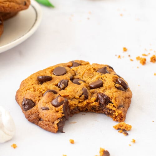caramel chocolate chip cookie with homemade caramel with a bite taken out on a white marble countertop.