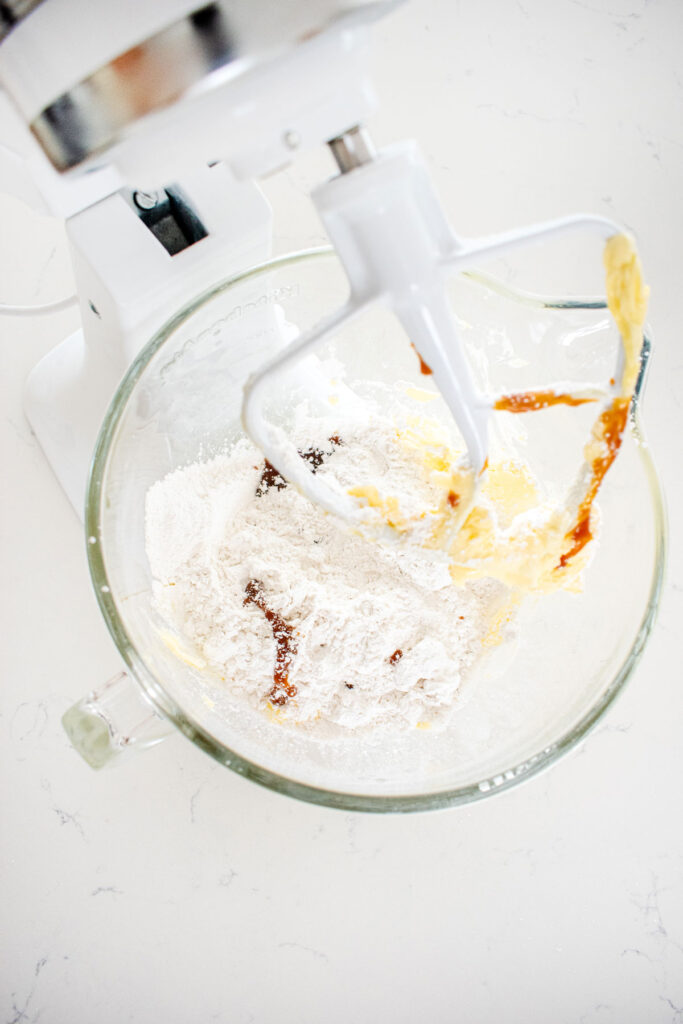 ingredients for caramel buttercream frosting in a glass stand mixing bowl on a white marble counter.