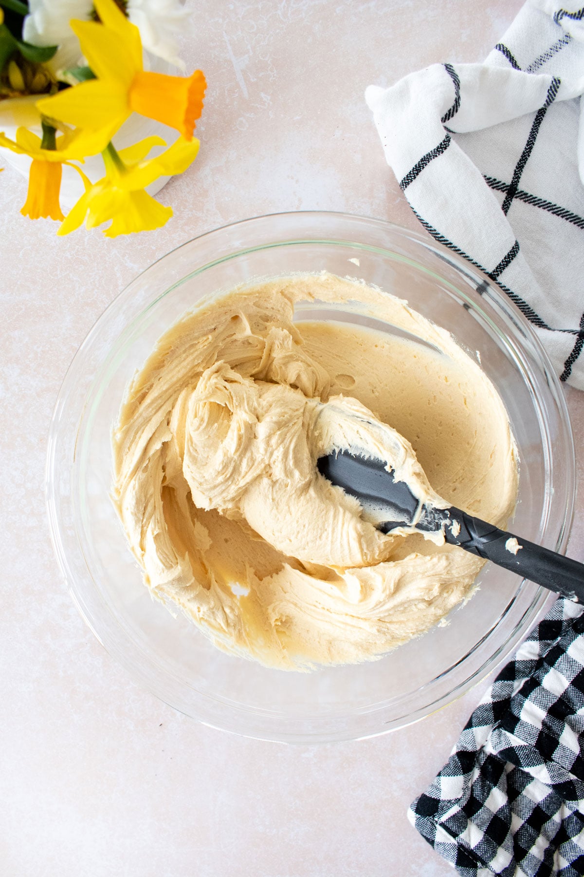 caramel buttercream frosting in a glass mixing bowl with a spatula on a tan counter.