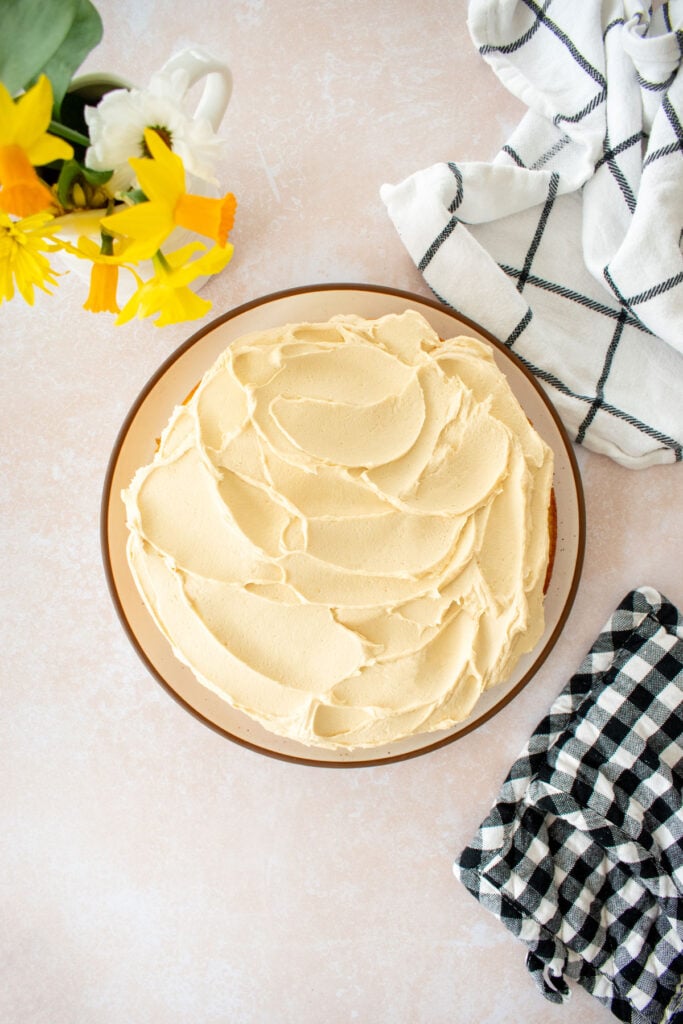 caramel buttercream frosting on a single layer cake on a plate on a tan counter with fresh flowers.