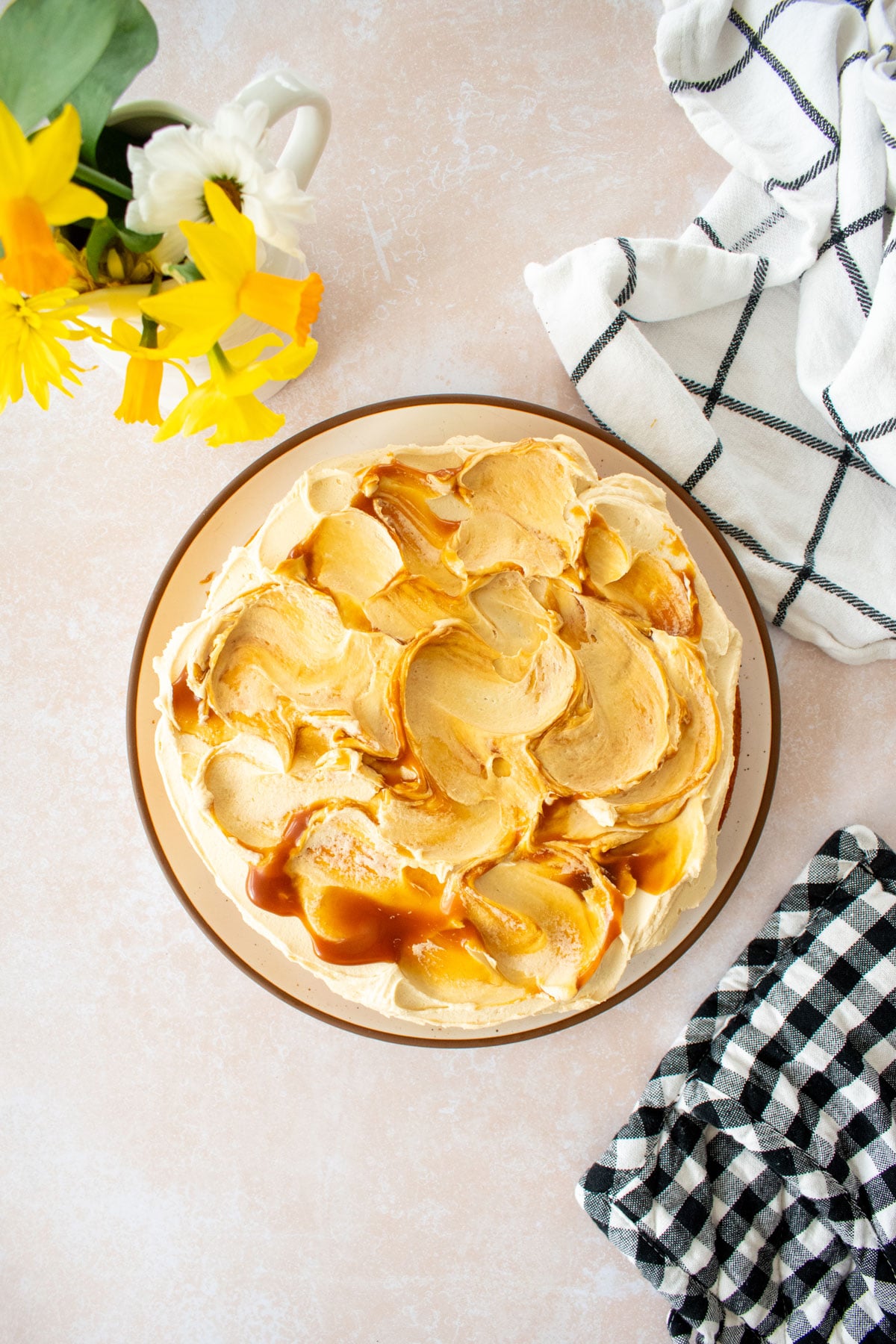 caramel buttercream frosting with caramel swirls on a single layer cake on a plate on a tan counter with fresh flowers.