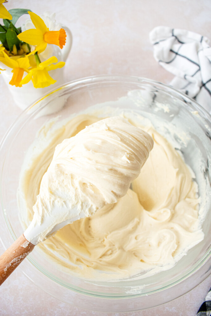 easy homemade cream cheese frosting on a spatula in a mixing bowl.