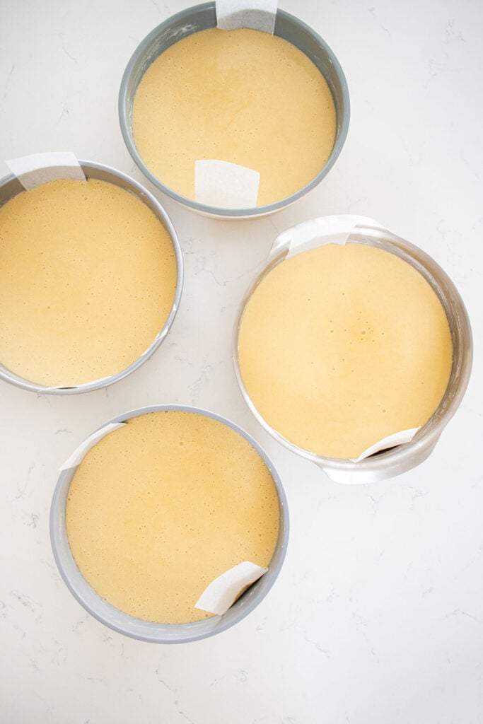 four different nontoxic cake pans test with vanilla cake batter inside each one on the counter.