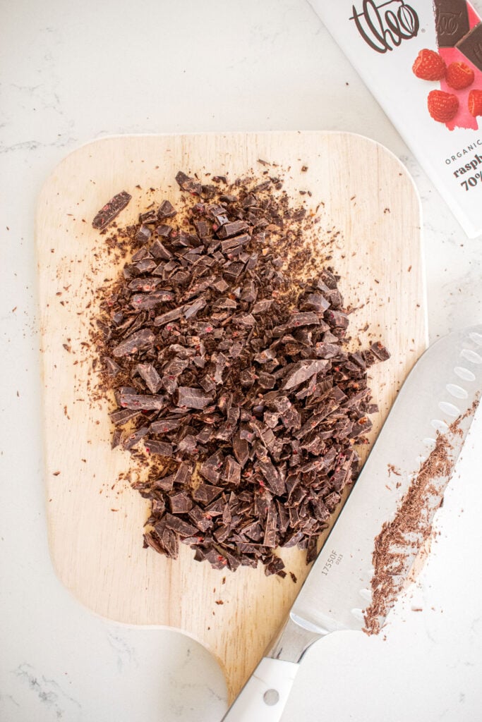 chopped dark chocolate bar on a wood cutting board on a marble counter.