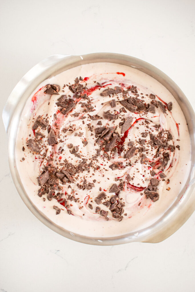raspberry no churn ice cream in a cake pan swirled with raspberry jam and dark chocolate chips.