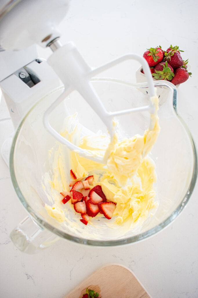softened butter and fresh sliced strawberries in a glass mixing bowl on a white marble countertop.