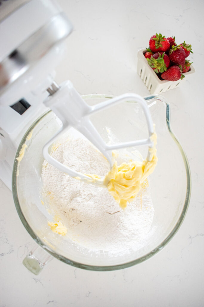 strawberry buttercream frosting ingredients in a glass mixing bowl ona white marble countertop.