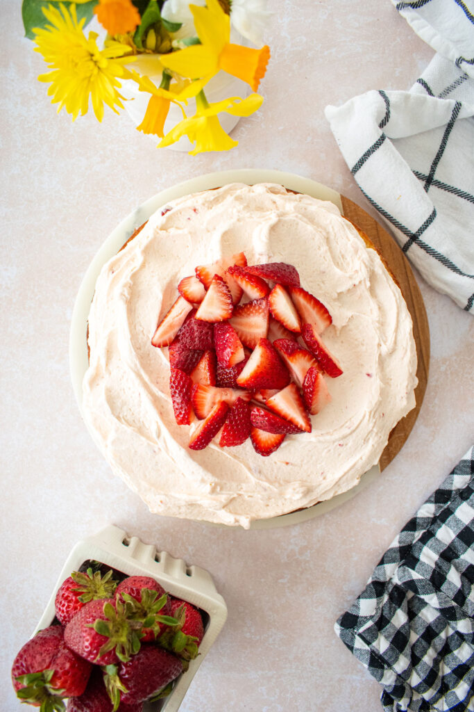 strawberry buttercream frosting on top of a single layer vanilla cake with fresh strawberries on top. 