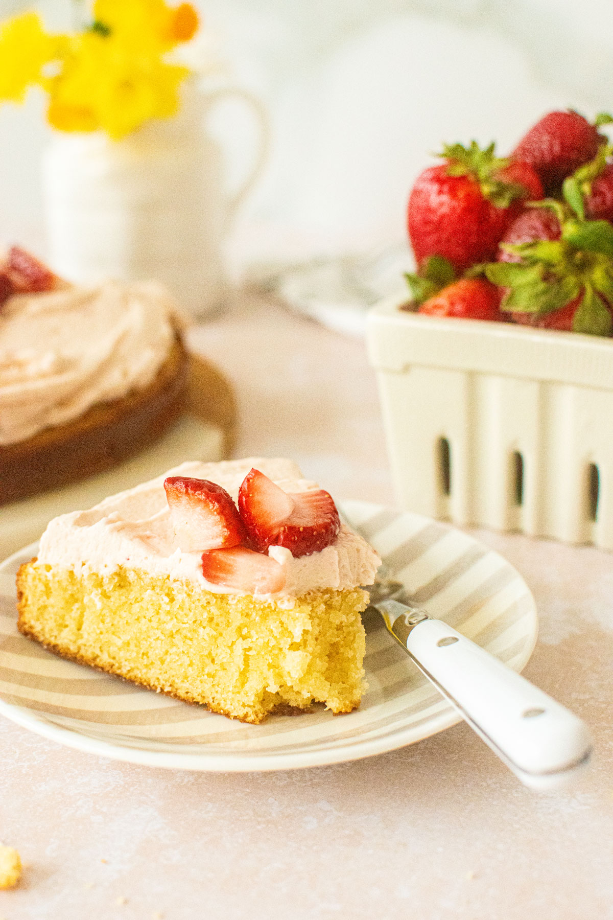 strawberry buttercream frosting on a vanilla cake slice on a striped cake plate with fresh strawberries on top.